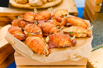 Mini Croissant Sandwiches with Ham and Greens. Close-up of small croissant sandwiches filled with ham and lettuce, served on parchment for catering or event presentation.