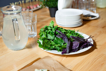Fresh herbs on plate for dinner preparation. Assorted fresh herbs including cilantro and purple basil arranged on a white plate, ready for cooking or serving at a dinner table.