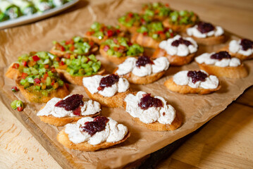 Assorted bruschetta with cream and vegetables. Close-up of crispy bruschetta topped with creamy spread and jam, alongside diced vegetable topping on toasted bread.