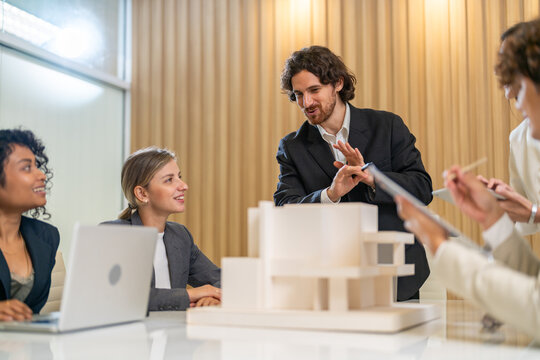 Architects engineers collaborating on building design project in modern office, diverse team of professionals female muslim architect and male engineers discussing architectural model of structure