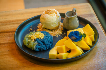 Mango sticky rice, a famous Thai dessert, served with two-color sticky rice, the purple color comes from butterfly pea flowers and the green color comes from pandan leaves.