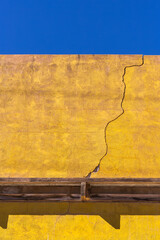 Yellow rendered wall with a large crack set against a blue sky