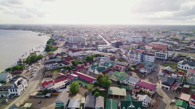 Drone flyover buildings in City of Paramaribo, Suriname river side, aerial view, camera tilt