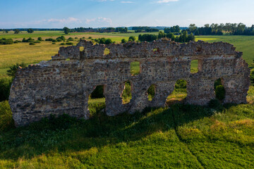 Fototapeta premium Ancient Stone Ruins of Laiuse Castle Standing in Verdant Estonian Countryside. Historic Medieval Fortress Surrounded by Lush Green Meadows and Golden Fields with Picturesque Rural Landscape Beyond