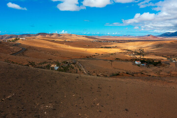 Panoramic View of Fuerteventura's Golden Desert Under Vibrant Blue Sky. Dramatic Arid Terrain of Canary Islands with Rolling Hills, Distant Mountains and Sparse Vegetation Against Azure Horizon