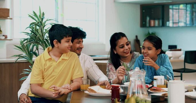 Indian Asian young family of four, including loving parents, son, a daughter, joyfully having breakfast together at a dining table in a beautifully designed modern home, enjoying a healthy meal