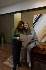 Fototapeta premium Two women in a modern art gallery examine artwork together during a casual afternoon gathering