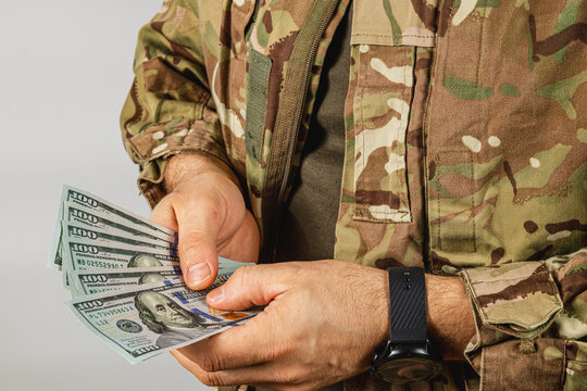 Soldier handles cash in camouflage attire at neutral location