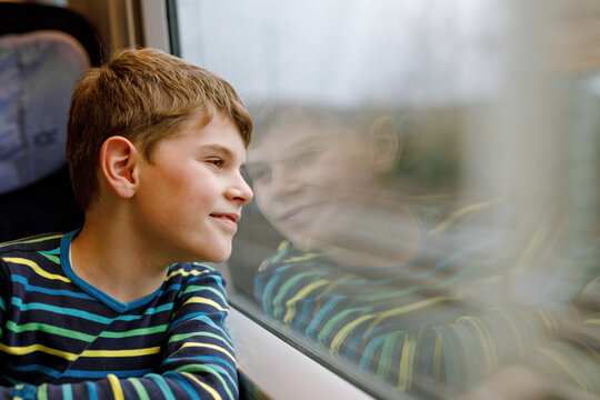 Adorable kid boy traveling by train. Happy smiling child looking out of the window during train moving. Kid dreaming and wondering. Family vacations and journey trip.