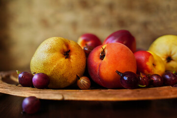 Close-up of ripe nectarines, pears, peaches and gooseberries on a carved wooden tray