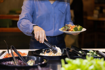 Close-up of a woman choosing vegetables at a salad bar