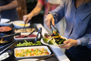 Close-up of a woman choosing vegetables at a salad bar