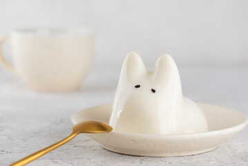 Vanilla jiggly cat dessert in a plate with cup of tea on a white table. Dancing jelly animal mousse panna cotta. Popular Korean, Japanese pudding.
