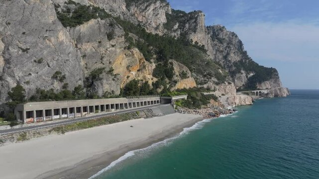 aerial with calm waters lapping the shoreline of Spiaggia del Malpasso, northern Italian beach and highway near the South of France