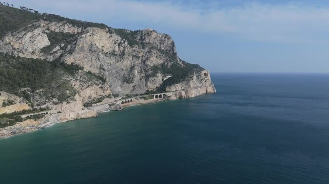 picturesque aerial from the sea inward showing the cliffside nooks and caves of the Spiaggia del Malpasso and highway travel,