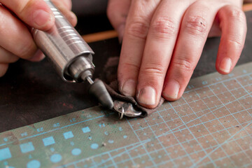 Close-up of hands of jeweler using a rotary tool to engrave a silver pendant on a cutting mat.