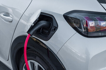 Fototapeta premium An electric car recharges its battery from a roadside charging point in the city