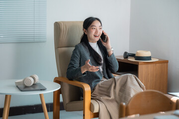 Businesswoman talking on phone and smiling while sitting on armchair