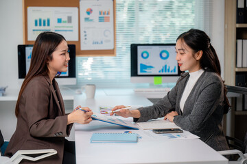 Two businesswomen analyzing financial charts and discussing data in office