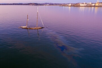 Sunken sailboat in the water, leaking oil into the harbor. Environmental pollution from a shipwreck...