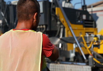 Construction worker standing and observing asphalt paver, ensuring quality on highway construction...