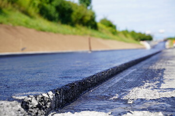 Detailed low-angle photo of new asphalt layer with bitumen coating, showcasing surface structure and thickness