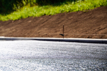 Low-angle shot of freshly laid asphalt layer with bitumen coating, showcasing surface texture and construction details