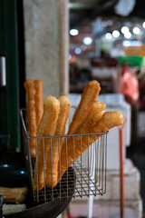 Freshly fried youtiao in a wire basket, ready to serve. Close-up of golden brown savory Asian fried bread snack.