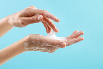 Fototapeta premium Woman washing hands with foaming soap on light blue background, closeup. Hygiene
