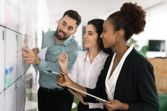 Positive diverse business team of young colleagues brainstorming at Kanban board, discussing scrum management method, working on project together, analyzing tasking plan - Powered by Adobe