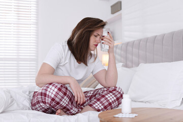 Fototapeta premium Unhappy woman with glass of water suffering from hangover on bed at home