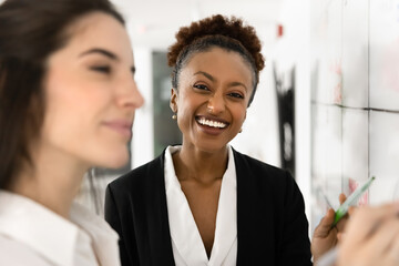 Cheerful beautiful young African businesswoman standing at whiteboard, looking at camera, posing...