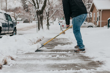 Adult man shovels snow off sidewalk on cold winter morning
