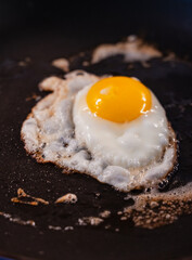 Close up of sunny-side up egg cooking in a black frying pan.