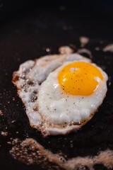 Close up of sunny-side up egg cooking in a black frying pan.