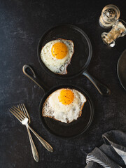 Top view fried eggs in pans with plate forks on black background.