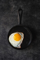 Top view of fried egg in cast iron frying pan on black background.