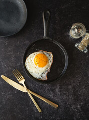 Top view fried egg in pan with plate cutlery on black background.