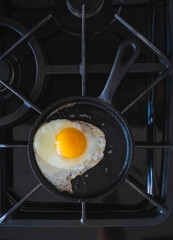 Top view of fried egg cooking in black frying pan on stove.
