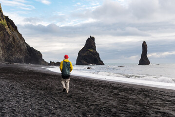 Man observes powerful waves and sea stacks at Reynisfjara, Vik