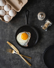 Top view fried egg in pan with plate cutlery on black background.