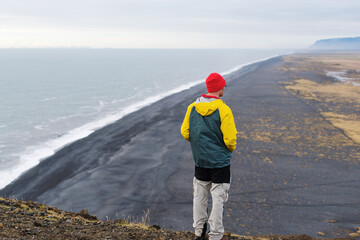 Man stands on cliff above iconic black sand beach in Iceland