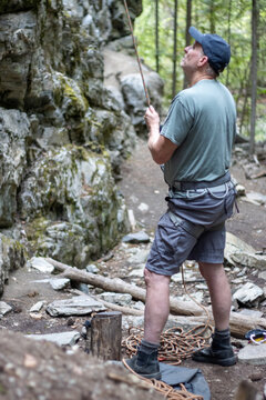 A rock climber holds a rigid rope while looking up a rugged cliff.