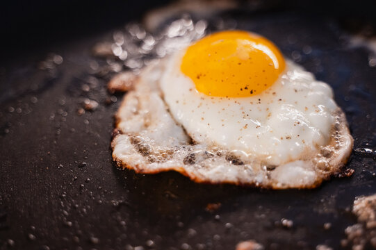 Close up of sunny-side up egg cooking in a black frying pan.