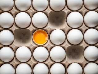 Top view of carton of white eggs with three missing and one broken.
