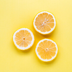 Overhead view of three slices of lemon on yellow background.