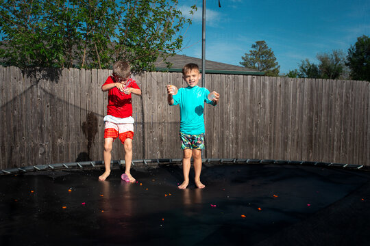 Two boys playing with water balloons on a trampoline in the sun