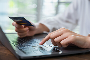Close-up of hand holding credit card and type on laptop keyboard with online payment for shopping.