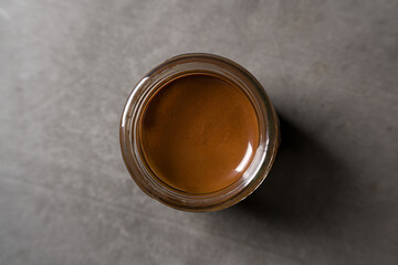 Top view of chocolate spread or nougat cream with hazelnuts in glass jar on dark background
