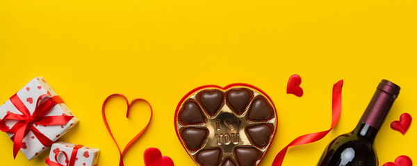 Bottle of red wine on colored background for Valentine Day with gift and chocolate. Heart shaped with gift box of chocolates top view with copy space
